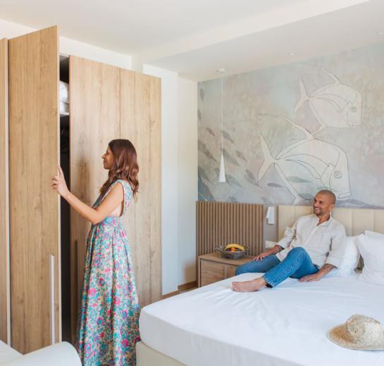 Couple in bedroom, she opens wardrobe, he sits on the bed.