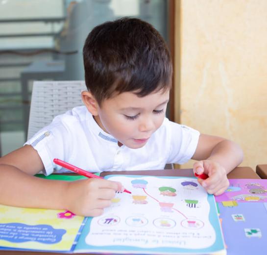 Child drawing with a red marker on a colorful book.